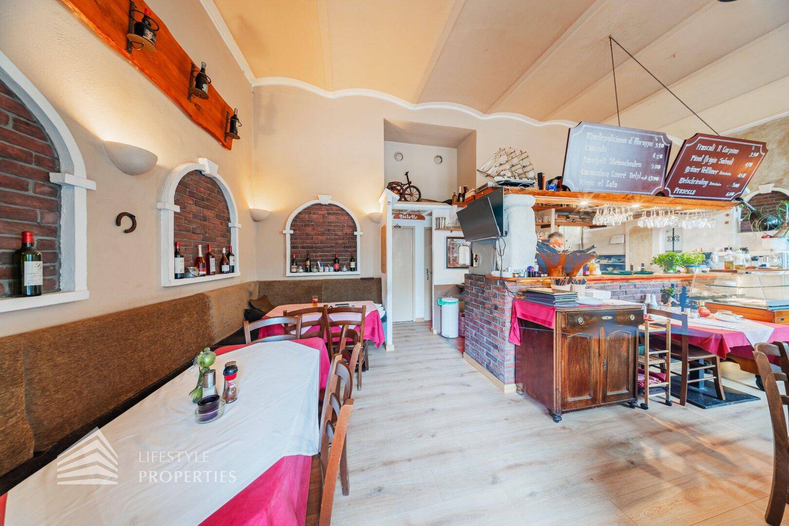 Übersicht des Restaurantbereichs mit Theke, Vitrine und Sitzgelegenheiten, geprägt von warmen Farben.