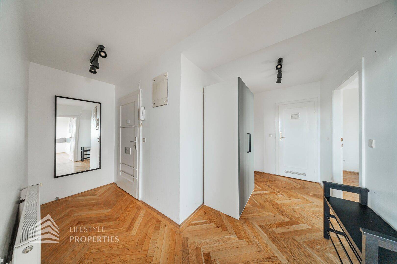 Eingangsbereich mit Spiegel, Garderobenschrank und Fischgrätparkett, der zu weiteren Räumen führt.