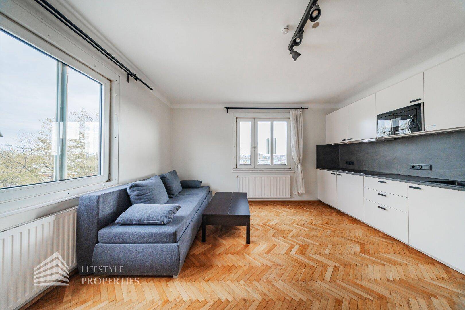 Offener Wohnbereich mit Küchenzeile, Sofa und zwei Fenstern für viel Tageslicht.