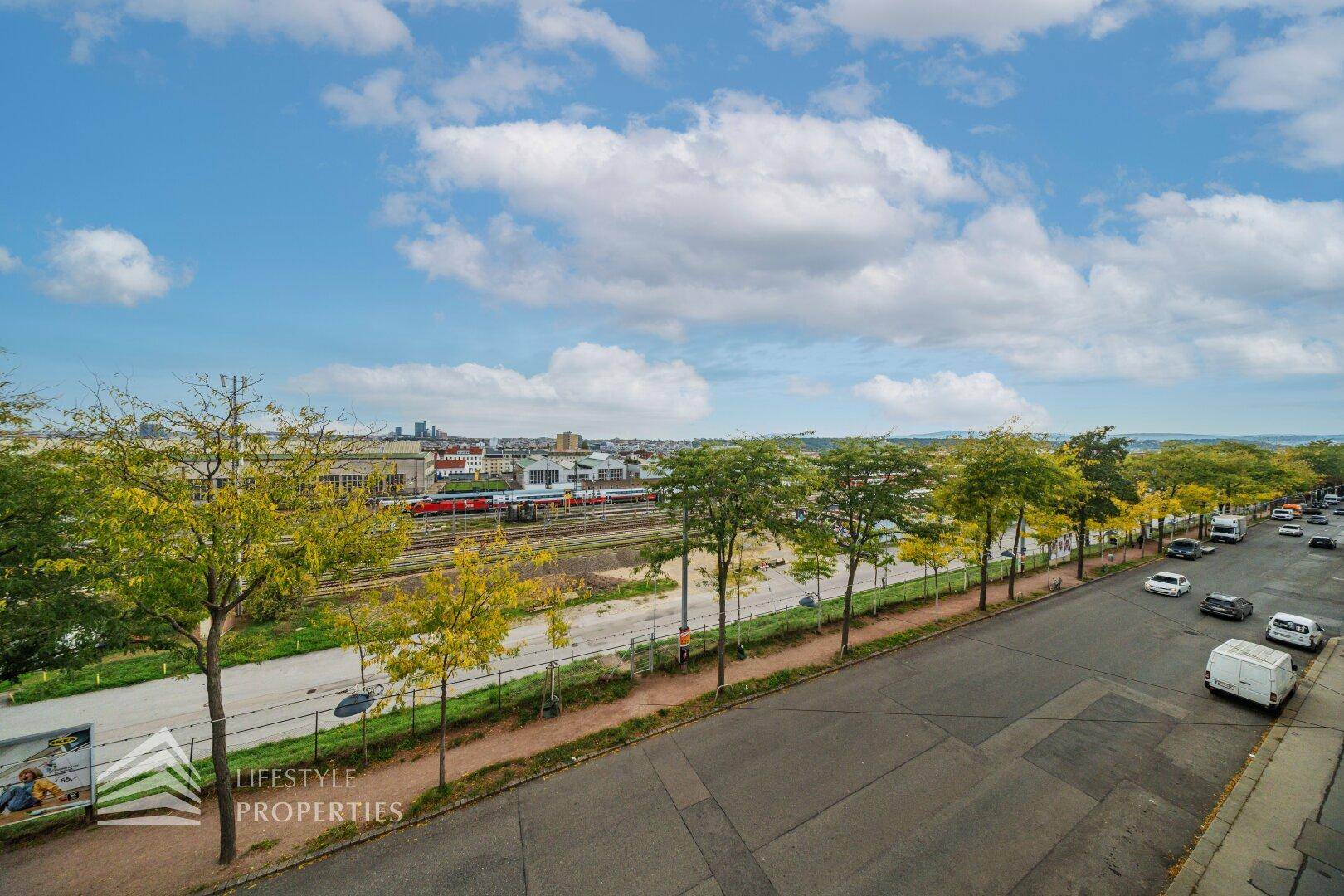 Weitblick über die Stadt mit Bahngleisen, Bäumen und einer belebten Straße.