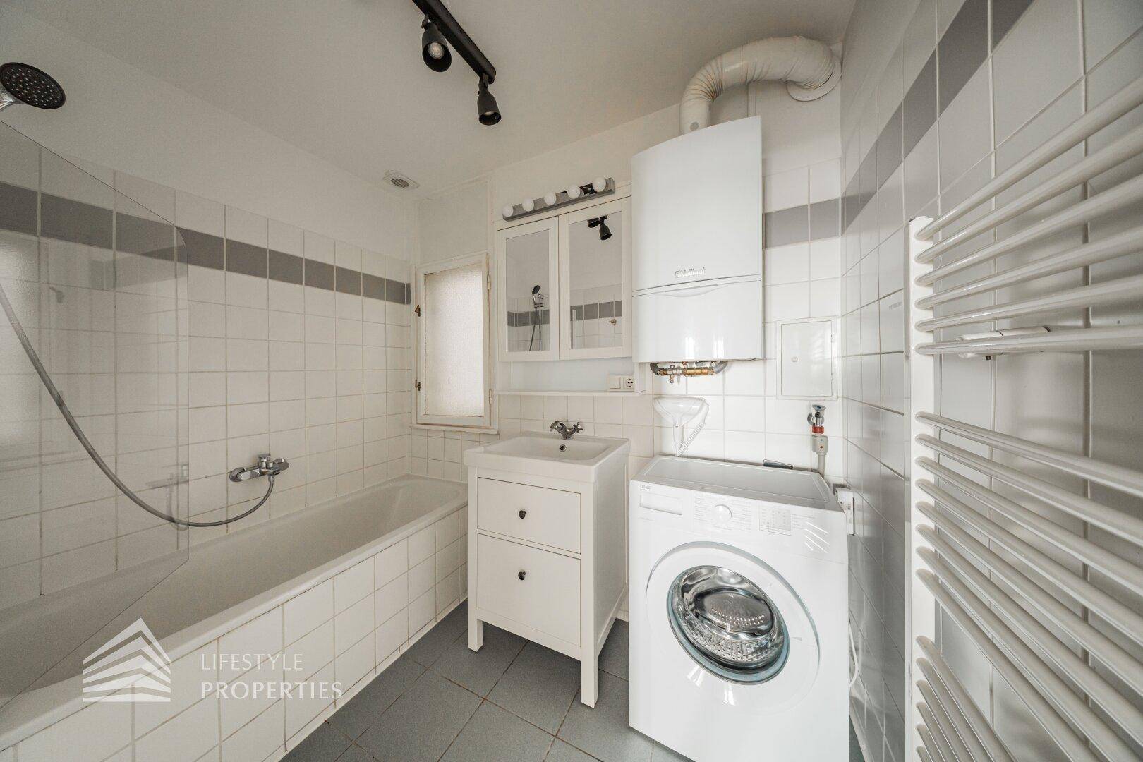 Badezimmer mit Badewanne, Waschmaschine, Waschbecken und beheiztem Handtuchhalter.