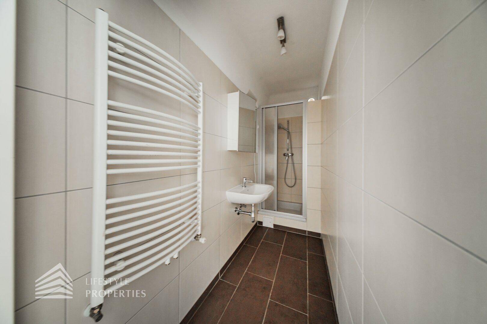 Modern gefliestes Badezimmer mit Dusche, Waschbecken und Handtuchheizkörper.