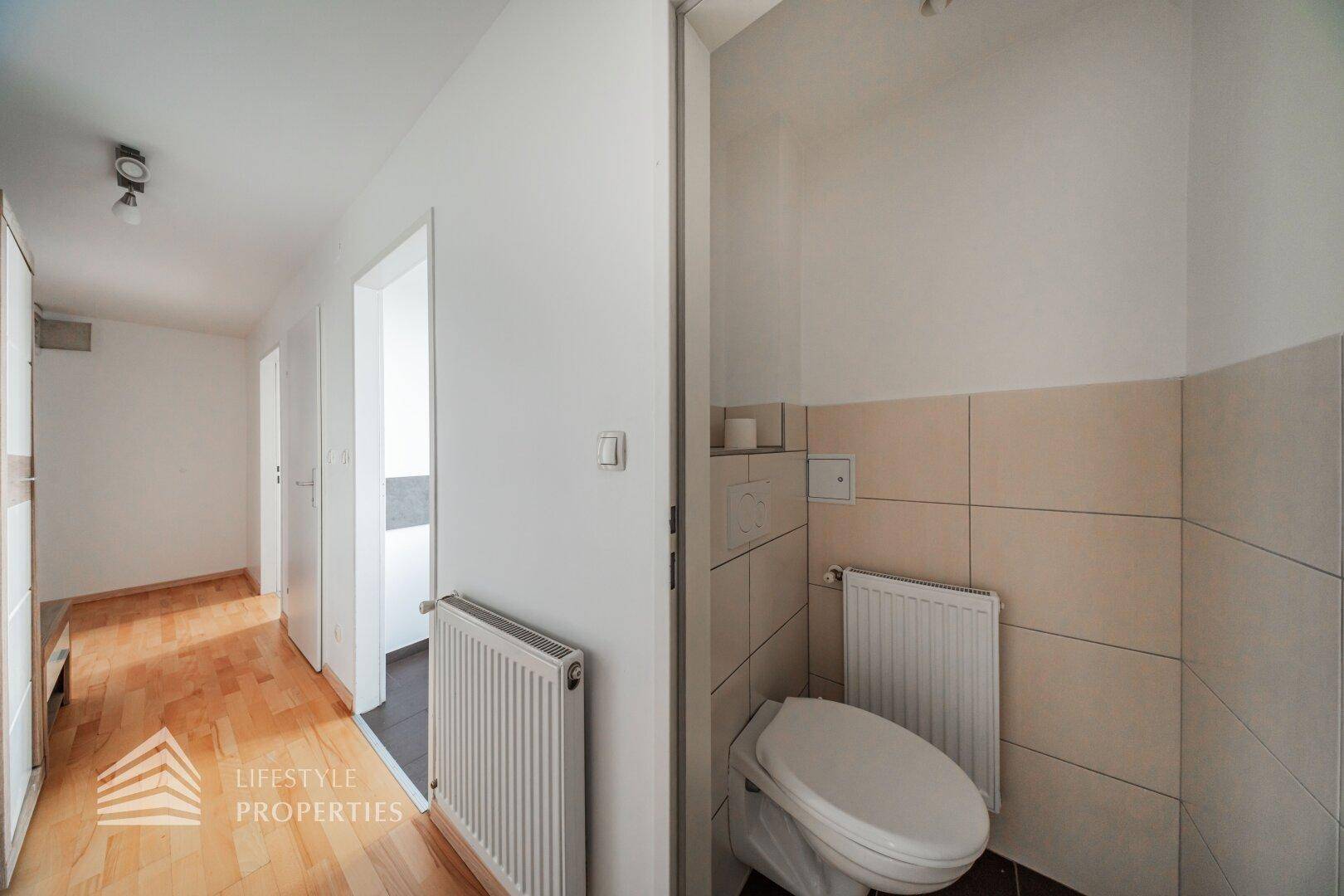 Separate Toilette mit Wand-WC, Heizkörper und Fliesen an den Wänden.