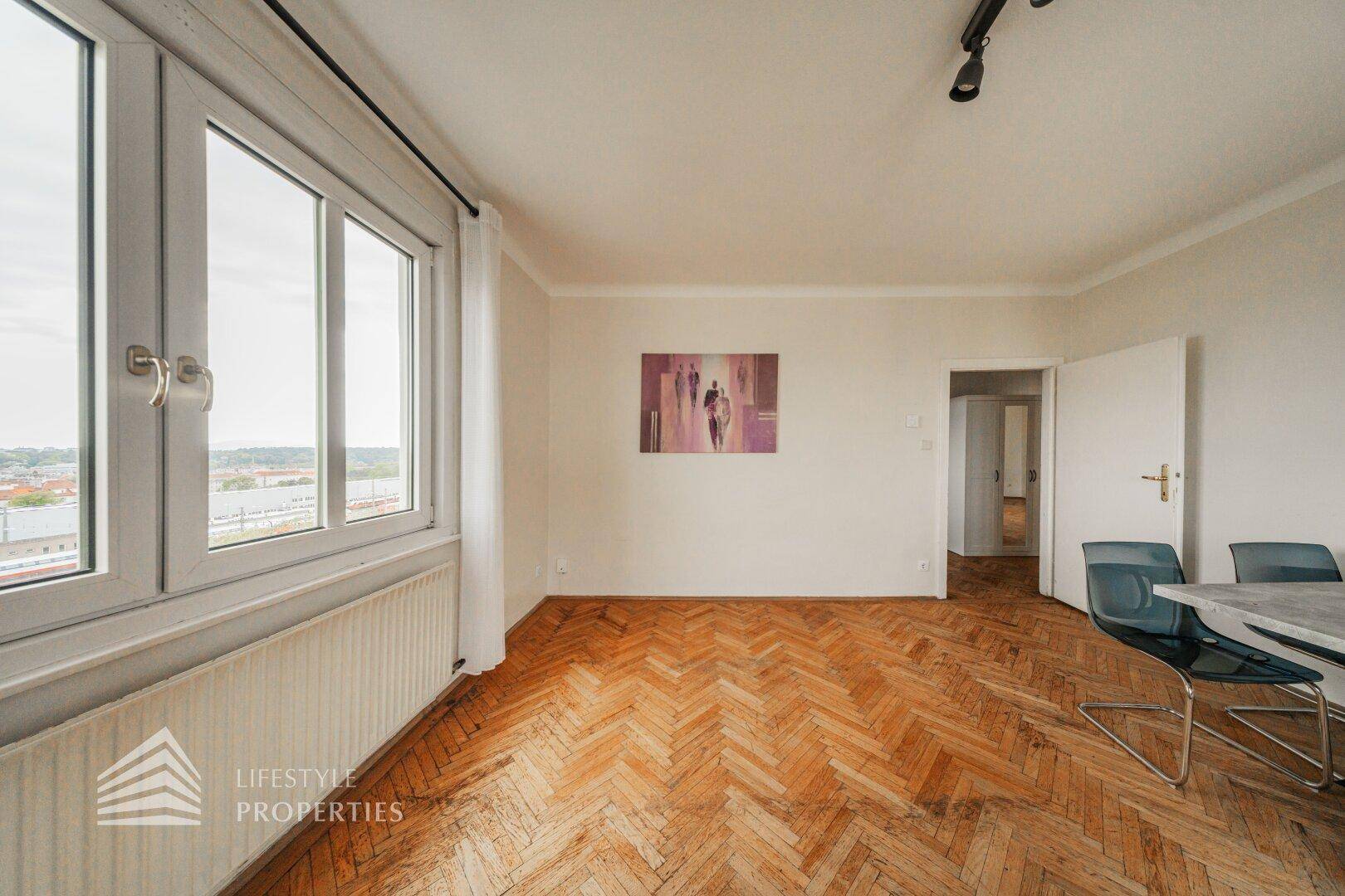 Geräumiger Wohnbereich mit Fischgrätparkett und Blick auf die Umgebung durch große Fenster.