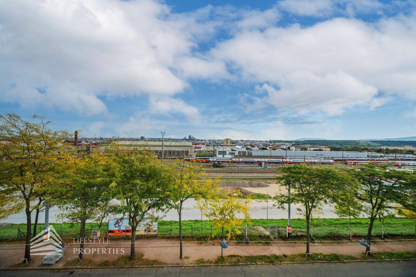 Weitläufiger Blick über Bahngleise und die Stadtlandschaft unter blauem Himmel.