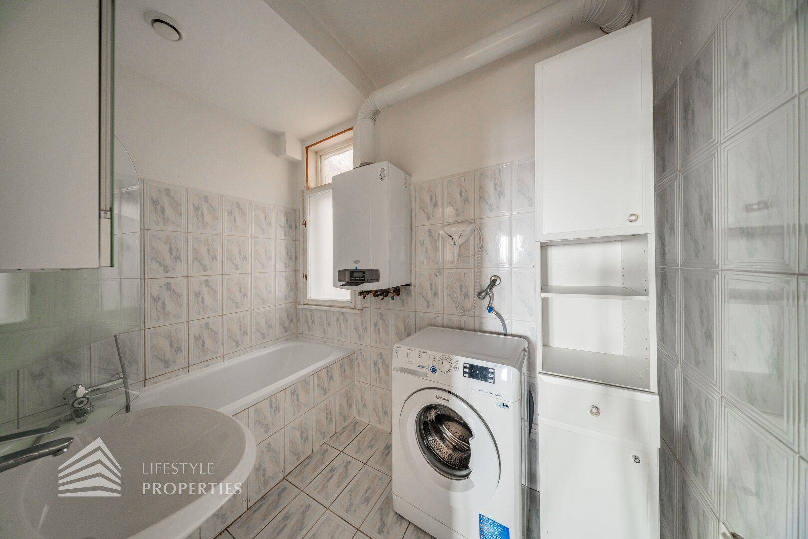 Gefliestes Badezimmer mit Badewanne, Waschmaschine und Fenster für Belüftung.