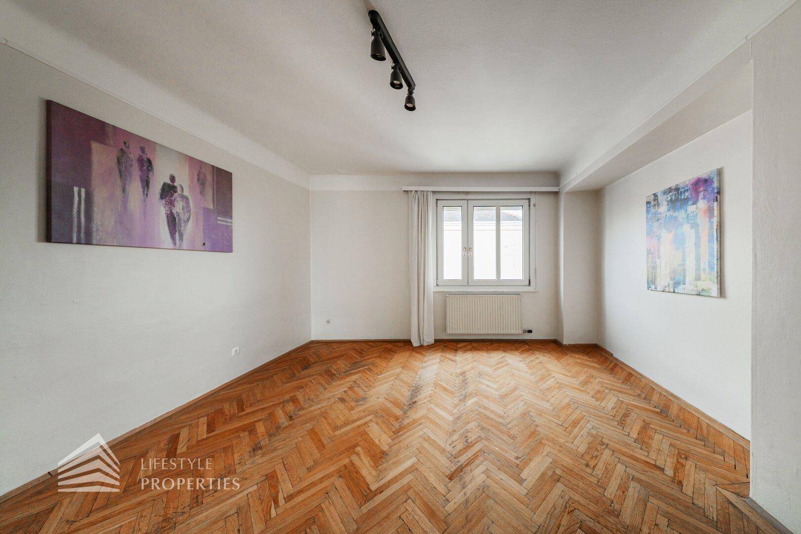Heller Wohnraum mit Fischgrätparkett und einem Fenster, das viel Tageslicht hereinlässt.