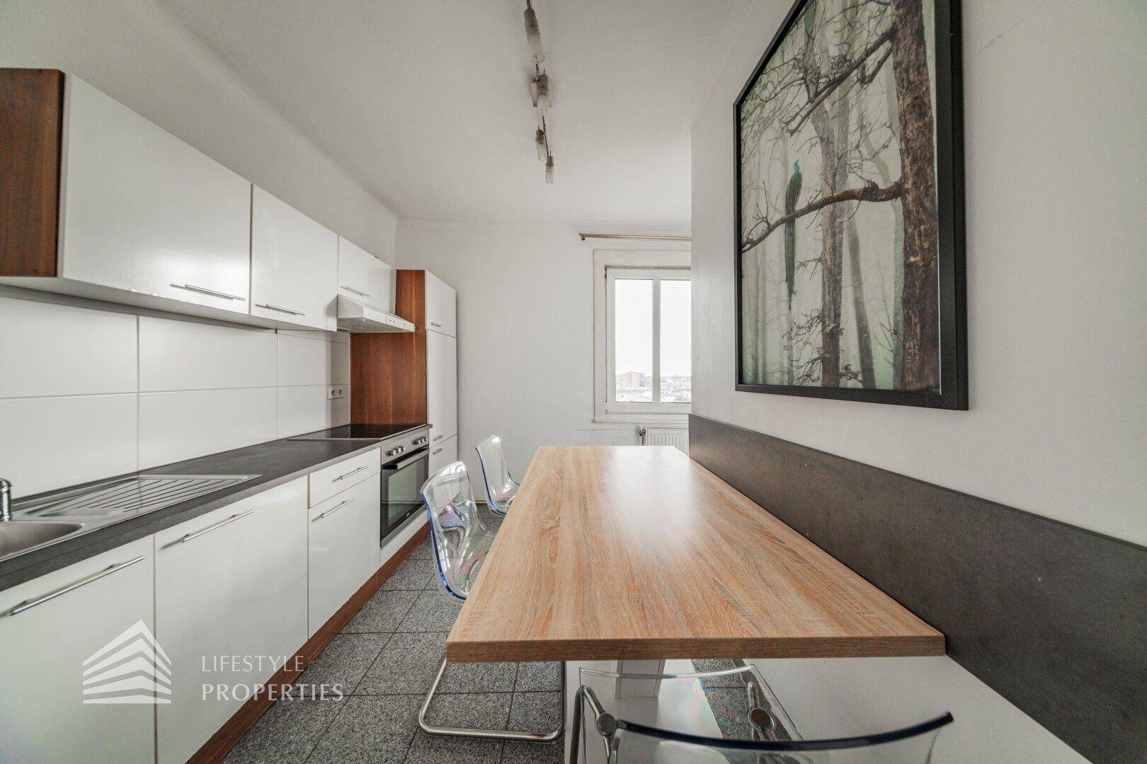 Moderne Einbauküche mit weißen Schränken, Essbereich und Fenster.