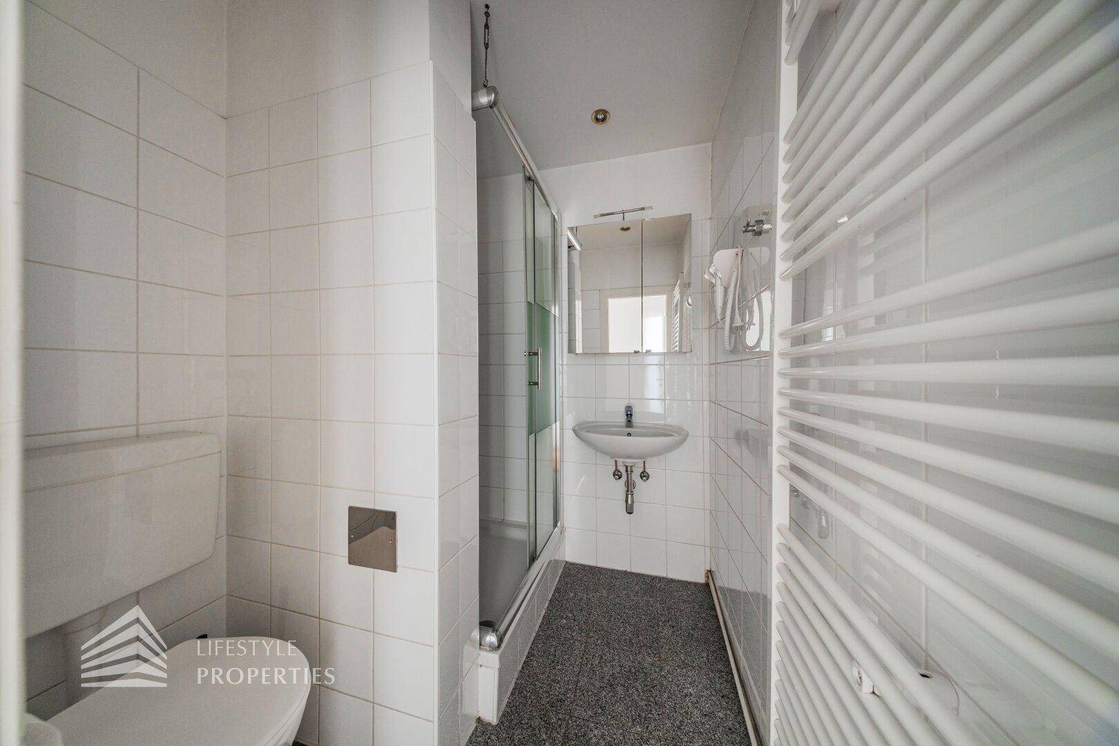 Funktionales Badezimmer mit Dusche, WC, Waschbecken und beheiztem Handtuchhalter.