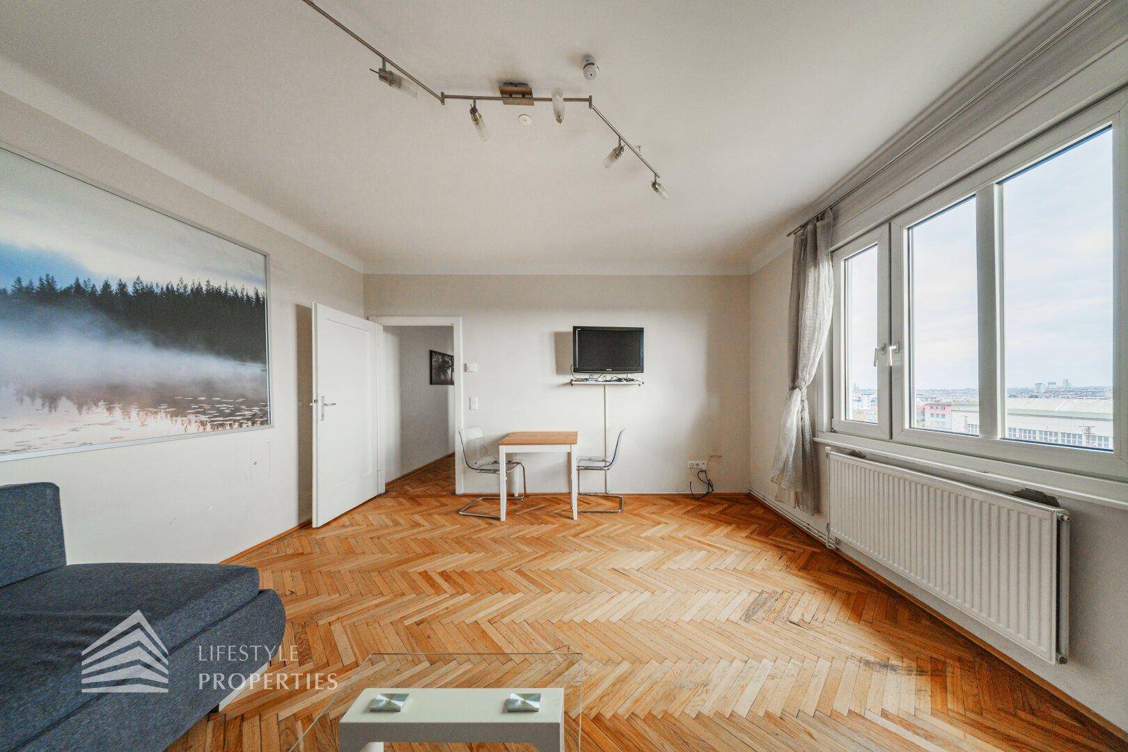 Geräumiger Wohn-Essbereich mit Parkettboden, Sofa und Essplatz am Fenster.