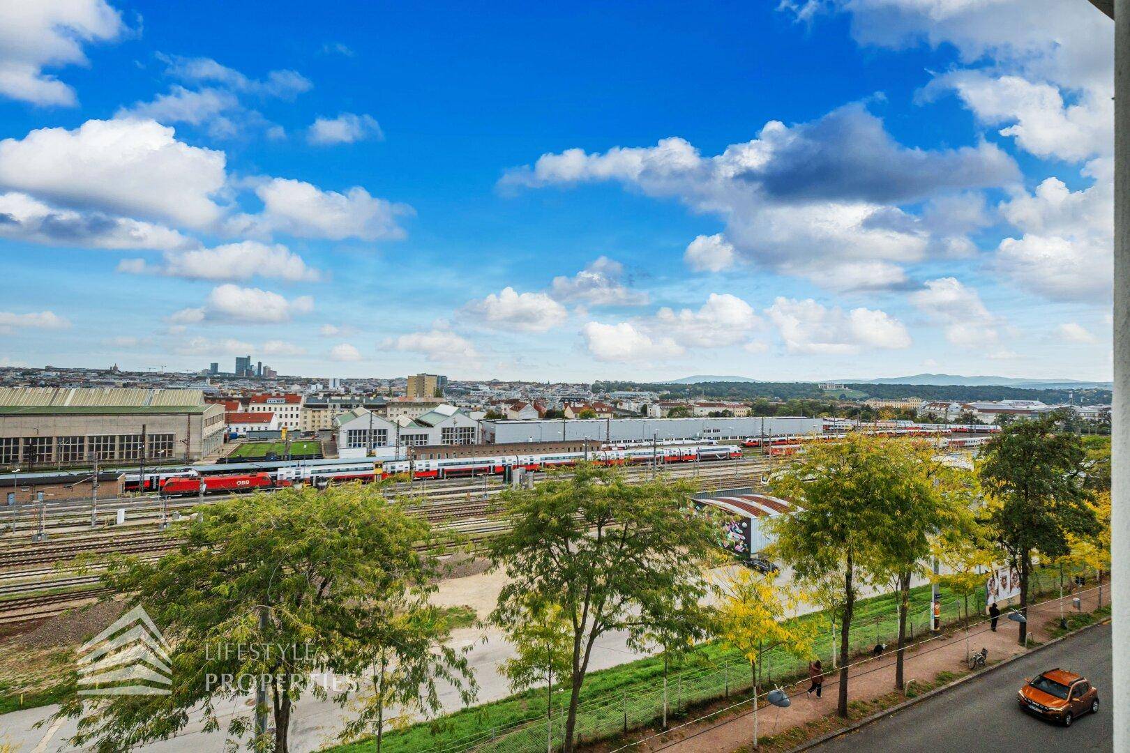 Weitläufige Aussicht über Bahngleise und die Stadtlandschaft unter blauem Himmel.