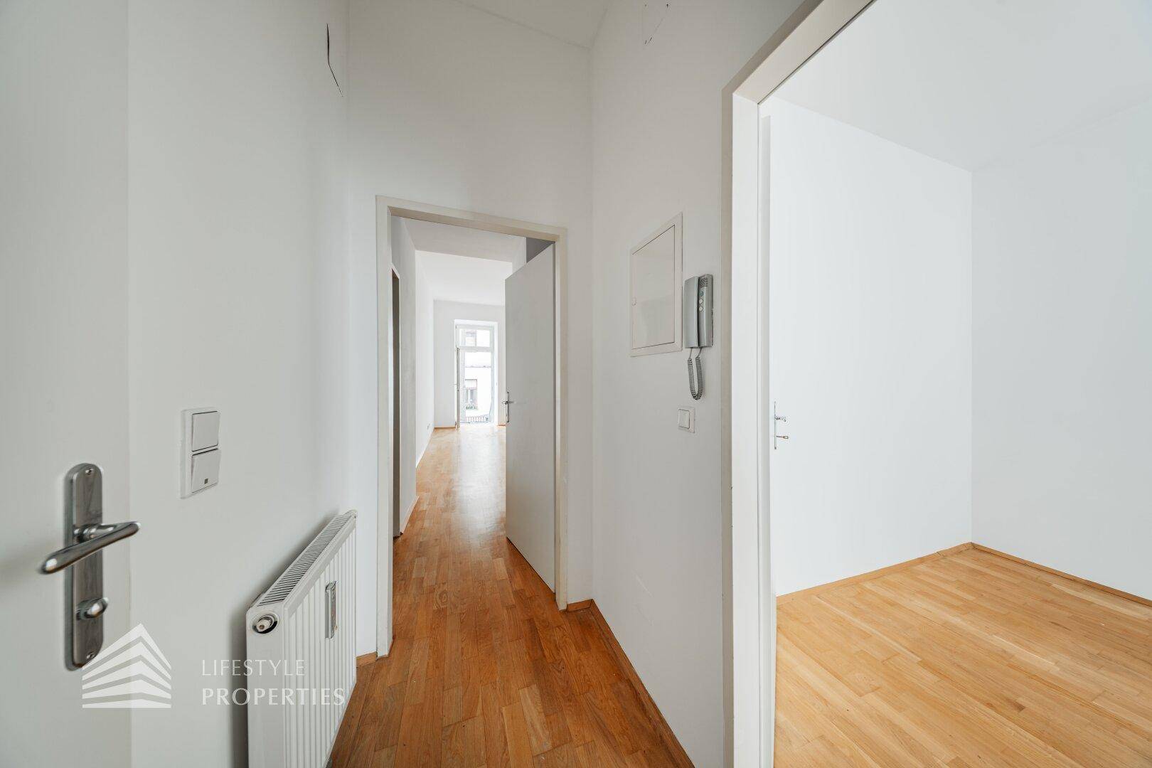 Heller Flur mit Holzboden und weißen Wänden, verbindet verschiedene Räume.