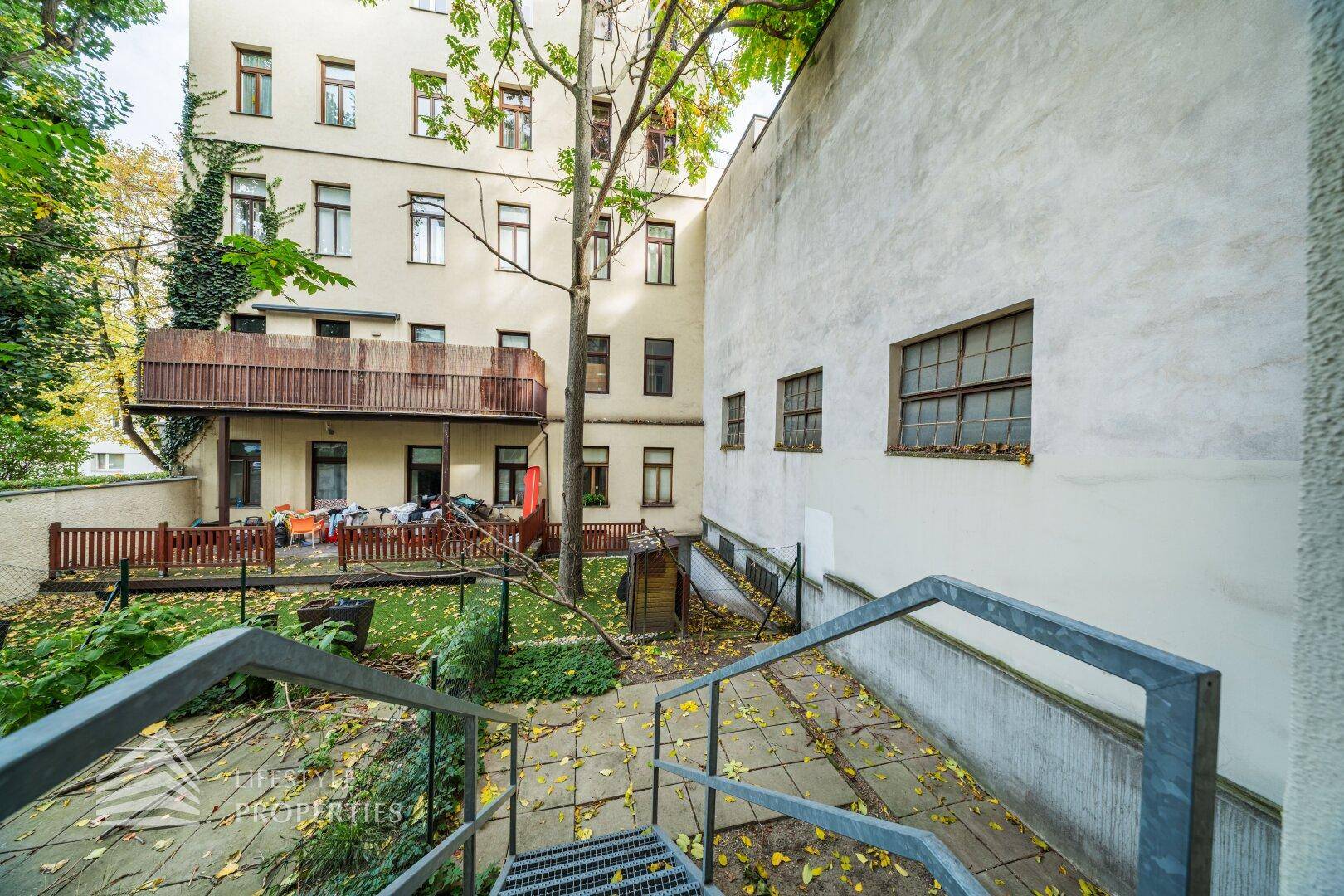 Hinterhof mit Treppen, Gartenbereich und einem Balkon im oberen Stockwerk.