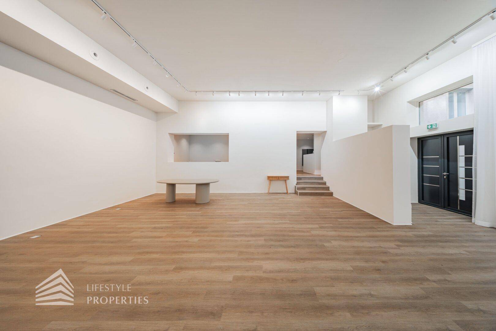 Heller Mehrzweckraum mit Holzboden, Treppe und einem runden Tisch, perfekt für flexible Gestaltung.