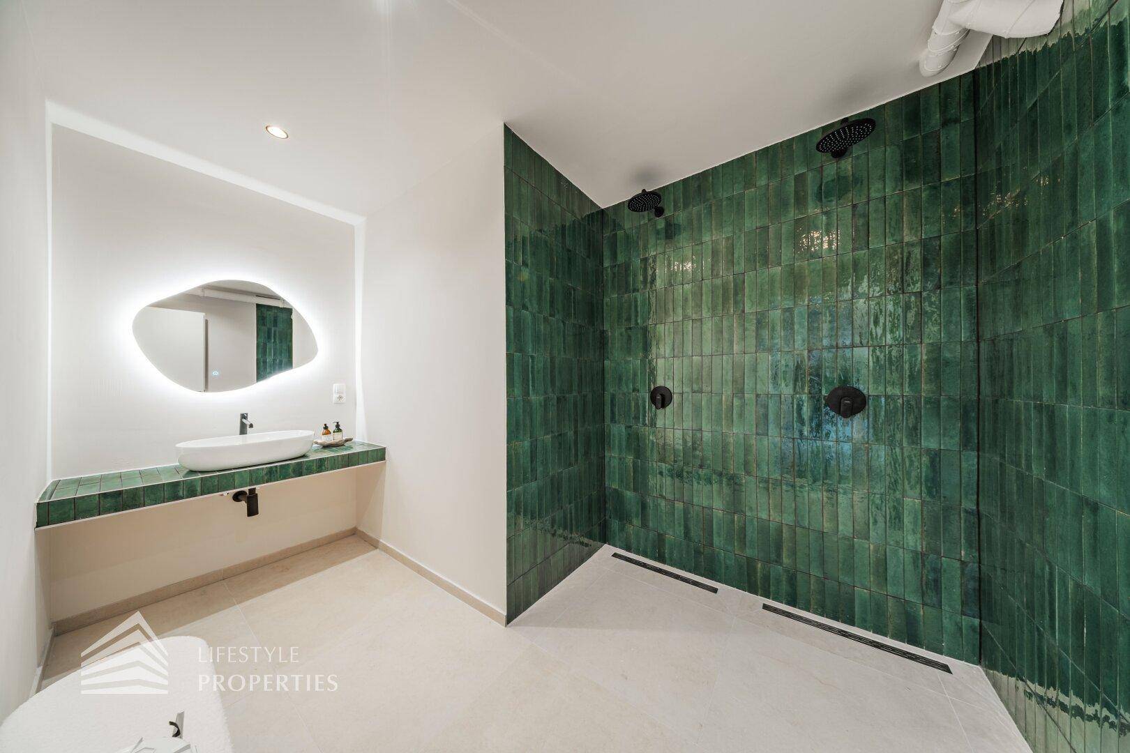 Modernes Badezimmer mit grünen Fliesen, großer Dusche und beleuchtetem Spiegel, stilvoll und funktional.