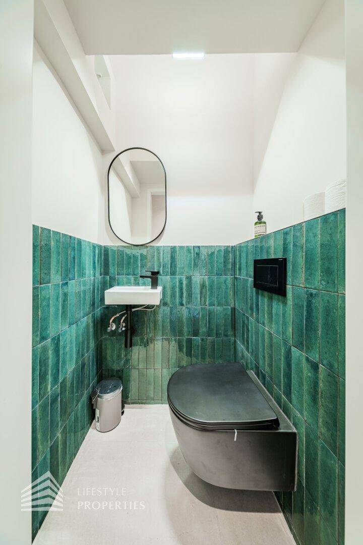 Stilvolle Gästetoilette mit grünen Fliesen, wandhängendem WC und kleinem Waschbecken, sehr gepflegt.