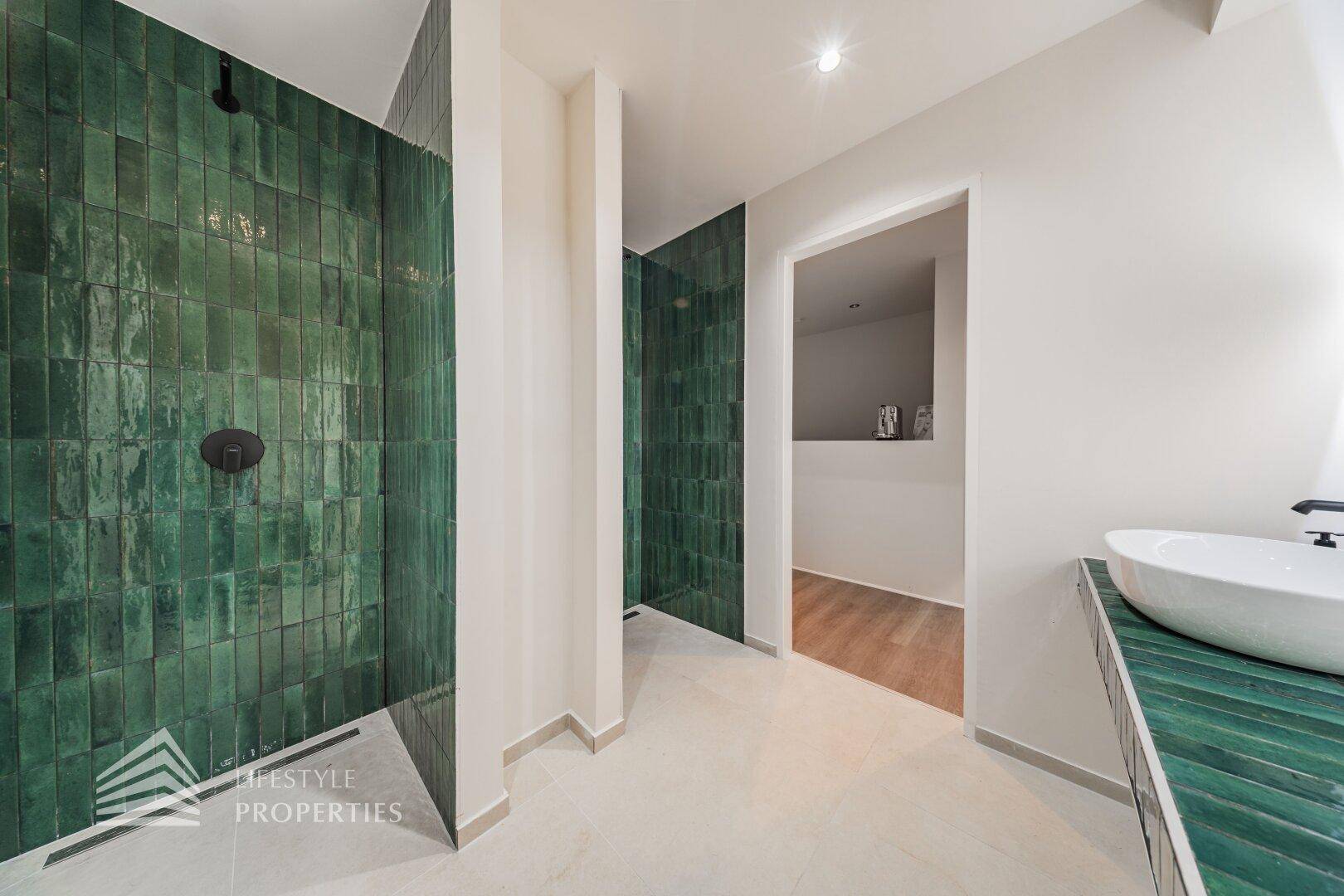 Modernes Badezimmer mit grünen Fliesen, Dusche und Waschtisch mit Aufsatzbecken, elegant und praktisch.