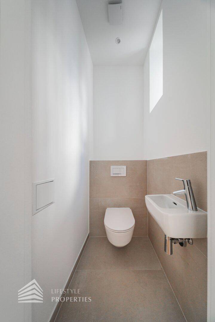 Modernes Gäste-WC mit wandhängender Toilette, kleinem Waschbecken und Fenster.