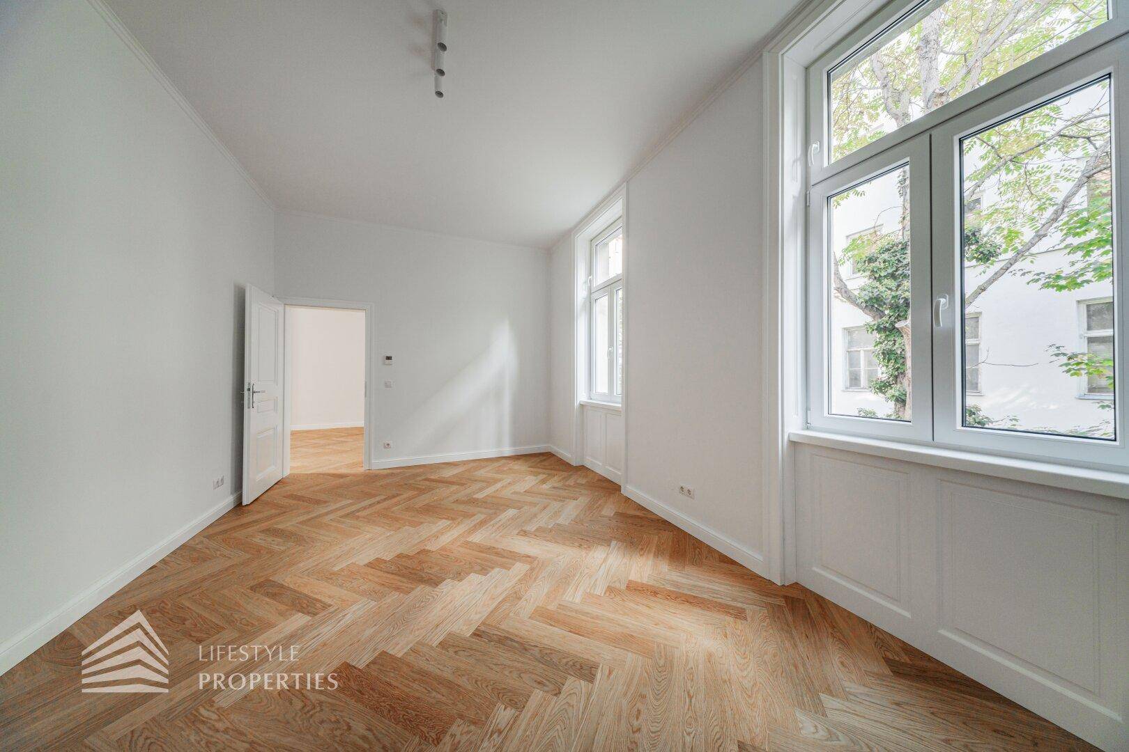 Heller Wohnraum mit Fischgrätparkett und großen Fenstern, die viel Tageslicht hereinlassen.