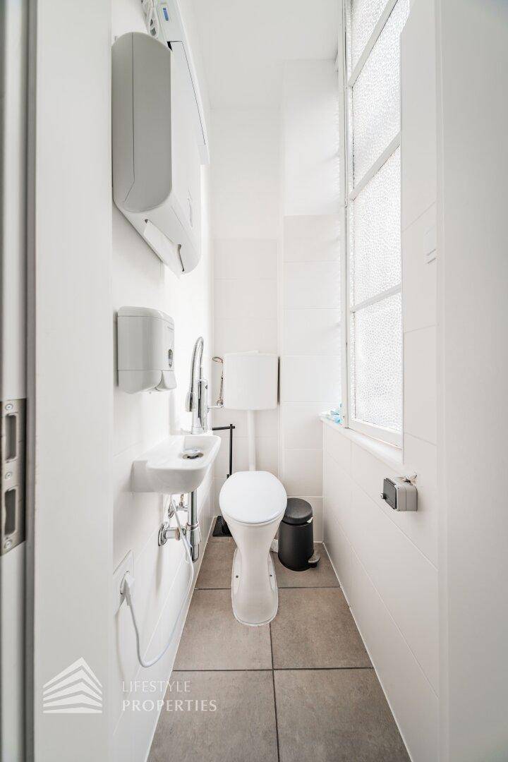 Saubere und funktionale Toilette mit Fenster, Waschbecken und Wandfliesen in hellem Design.