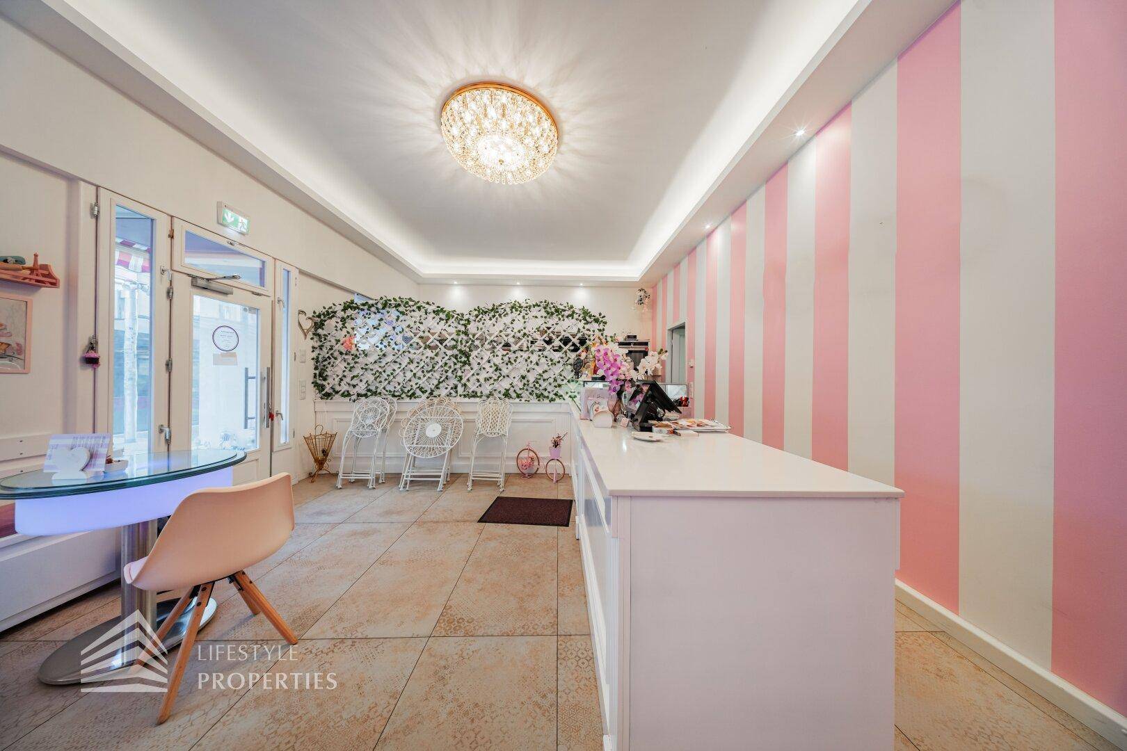 Heller Verkaufsraum mit rosa-weiß gestreiften Wänden, Sitzgelegenheiten und einer dekorativen Pflanzenwand, die den Raum belebt.