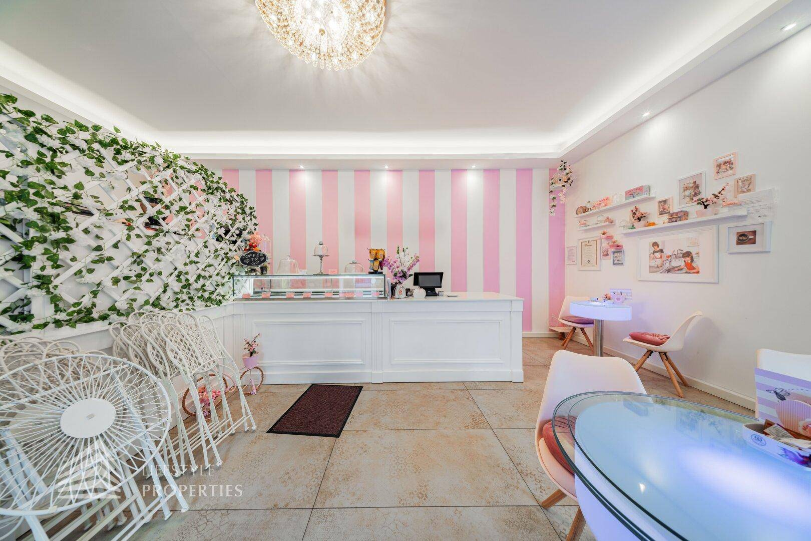 Einladender Verkaufsraum mit dekorativer Pflanzenwand, rosa-weiß gestreiften Wänden und einem eleganten Kronleuchter.