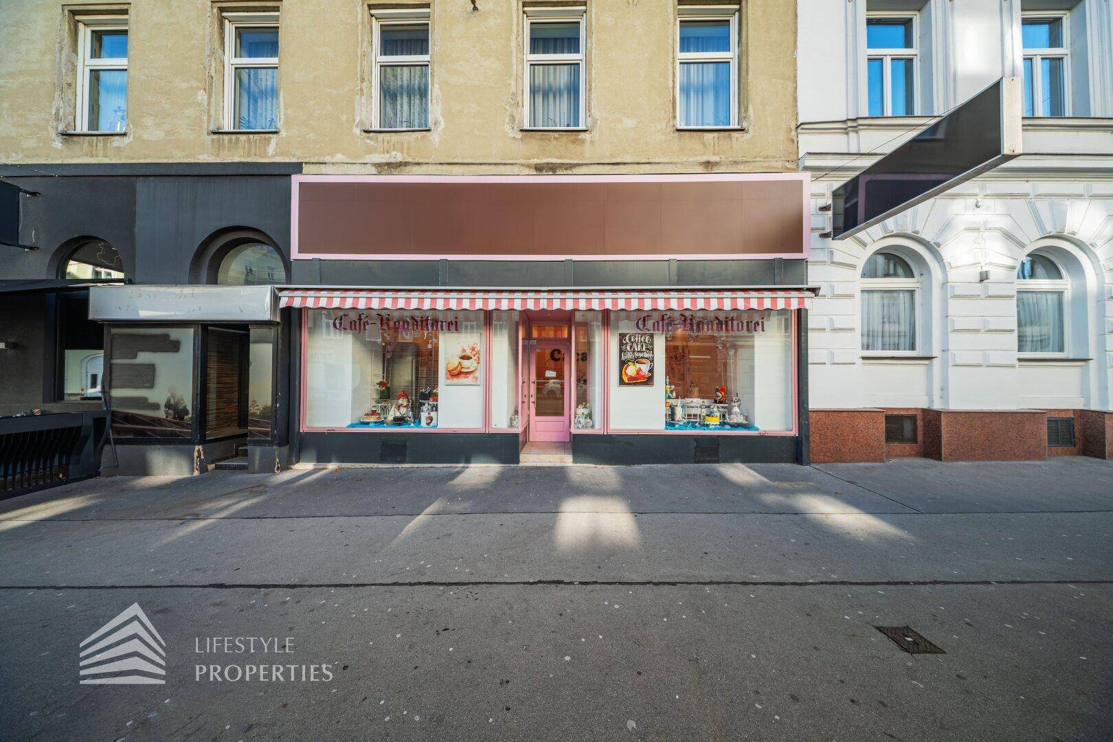 Attraktive Ladenfront eines Cafés mit Markise und großen Schaufenstern in einer belebten Straße, einladend gestaltet.