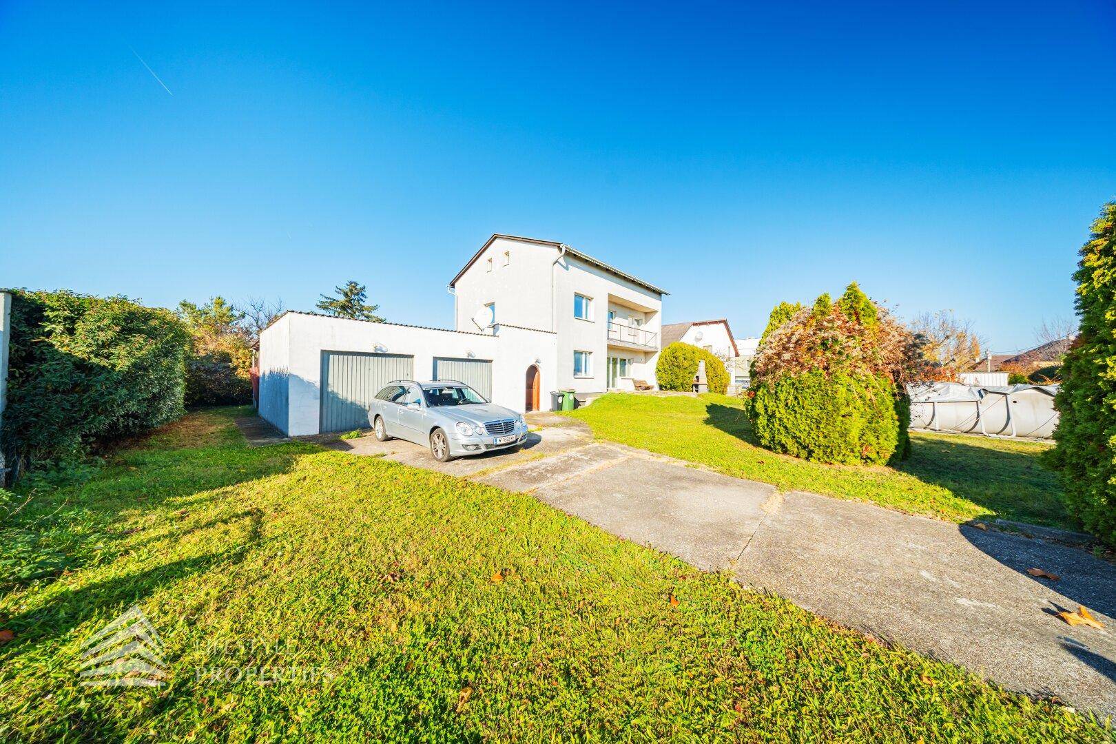 Vorderansicht des Hauses mit Zufahrt, Garagen und gepflegtem Vorgarten.