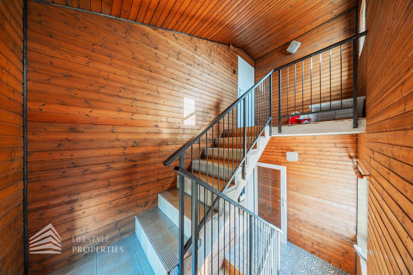 Treppenhaus mit Holzverkleidung an Wänden und Decke, sowie Metallgeländer.