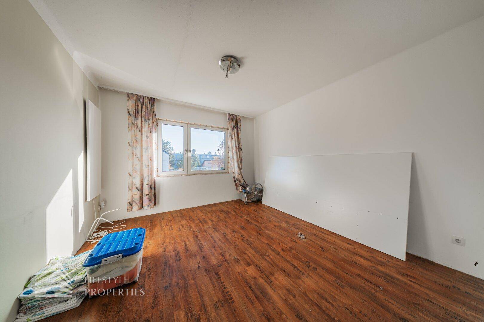 Leeres Zimmer mit Laminatboden und Fenster, bereit zur individuellen Gestaltung.