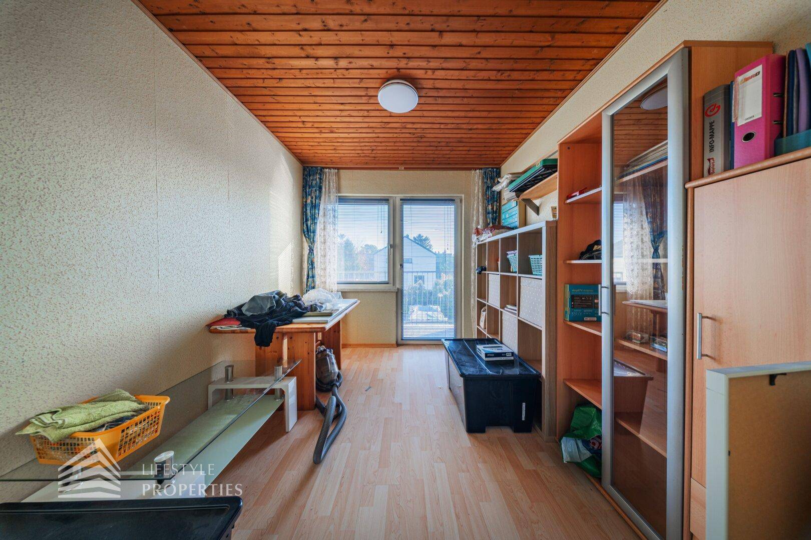 Zimmer mit Holzdecke, Laminatboden und Regalen, bietet Stauraum und Gemütlichkeit.