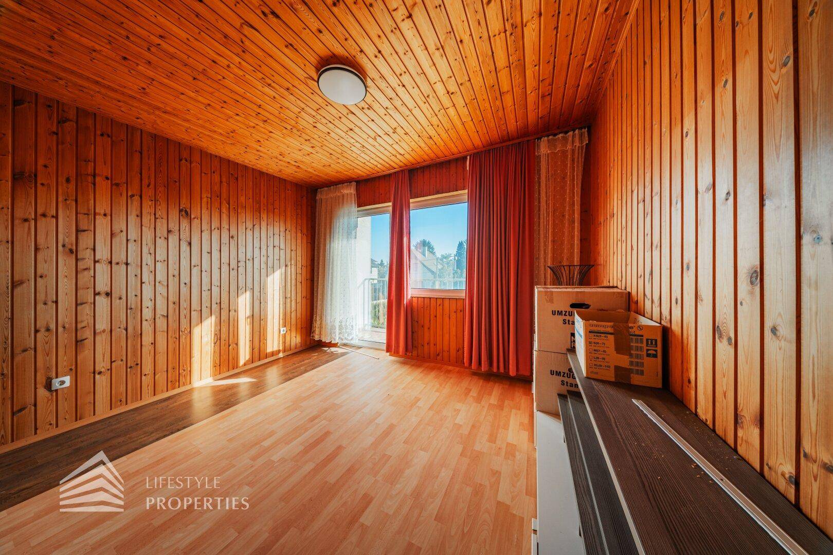 Gemütliches Zimmer mit viel Holz an Wänden und Decke, sowie Laminatboden.