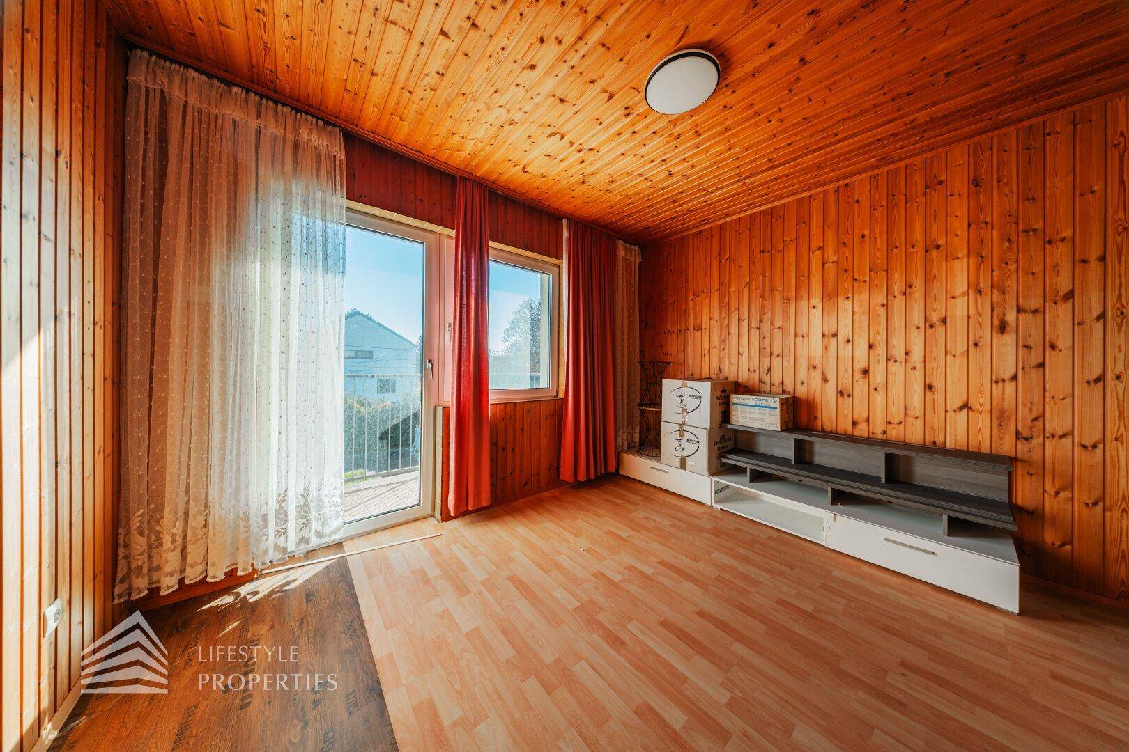 Zimmer mit Holzverkleidung, Laminatboden und direktem Zugang zum Balkon.