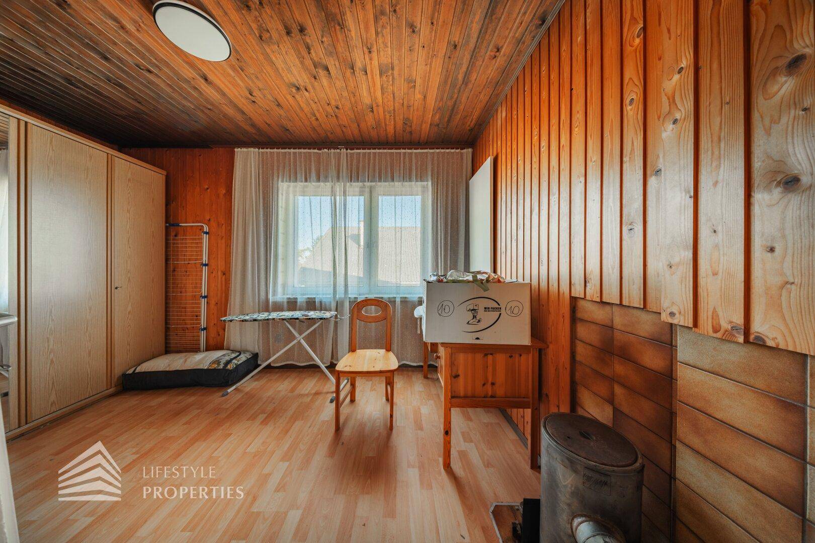 Zimmer mit Holzverkleidung, Laminatboden und Fenster, bietet eine warme Atmosphäre.