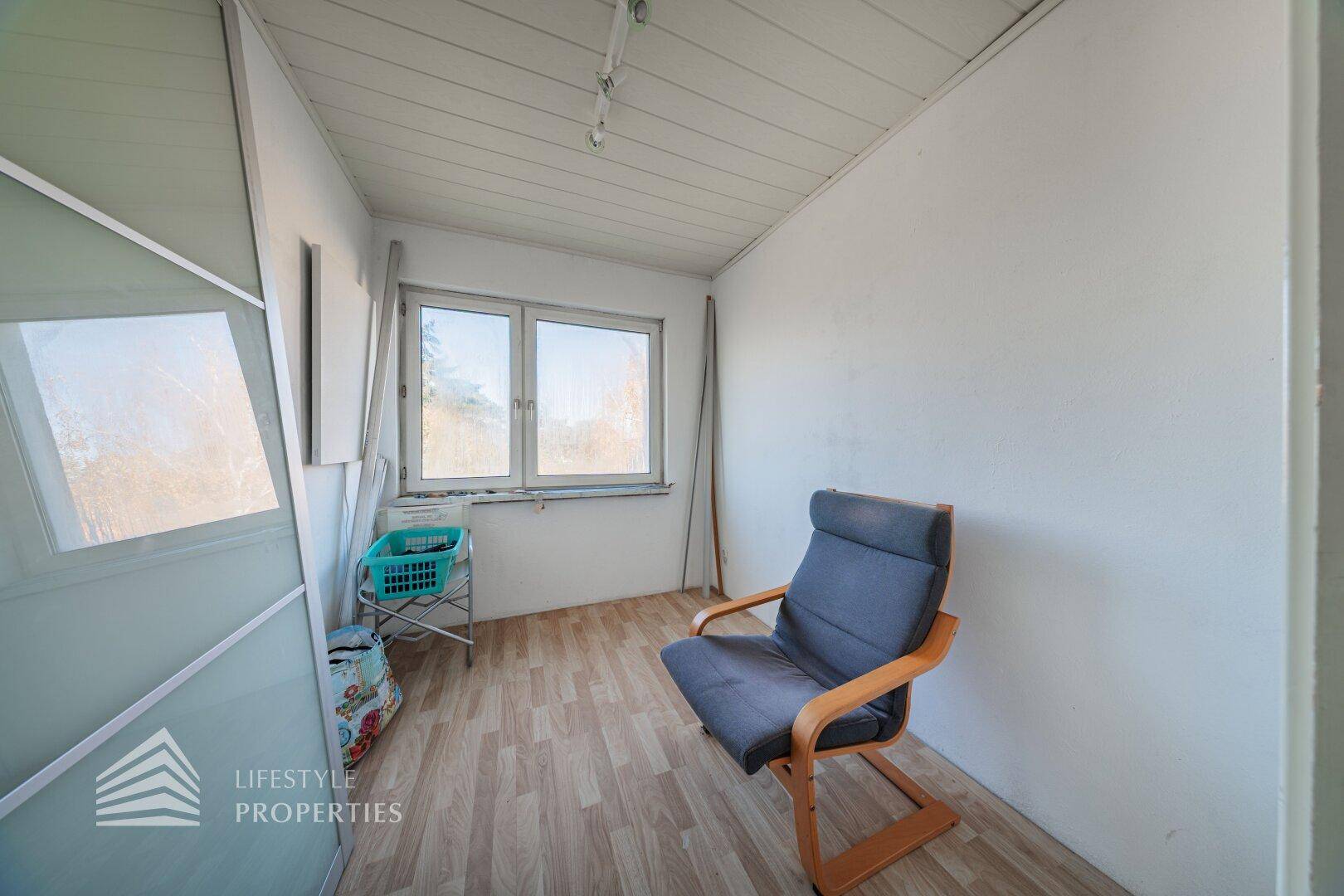 Kleiner Raum mit Laminatboden, Fenster und einem einzelnen Stuhl, ideal als Abstellraum.