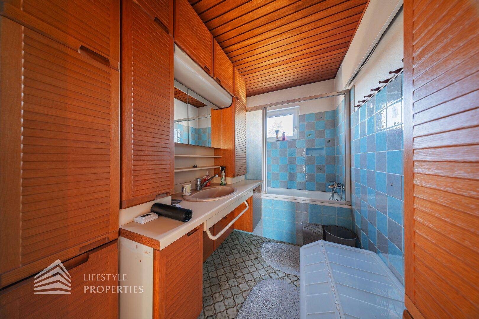 Badezimmer mit blauen und grauen Fliesen, Holzschränken und einer Badewanne.
