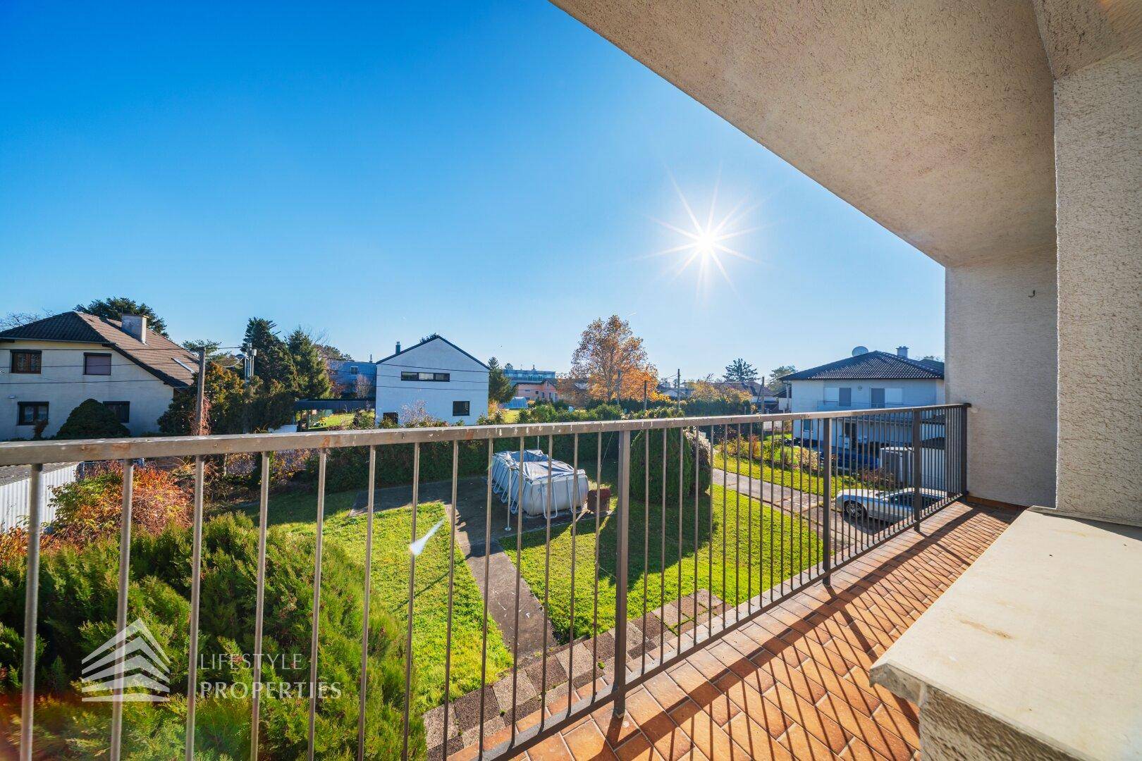 Sonniger Balkon mit Terrakottafliesen und weitem Blick über den Garten und die Umgebung.