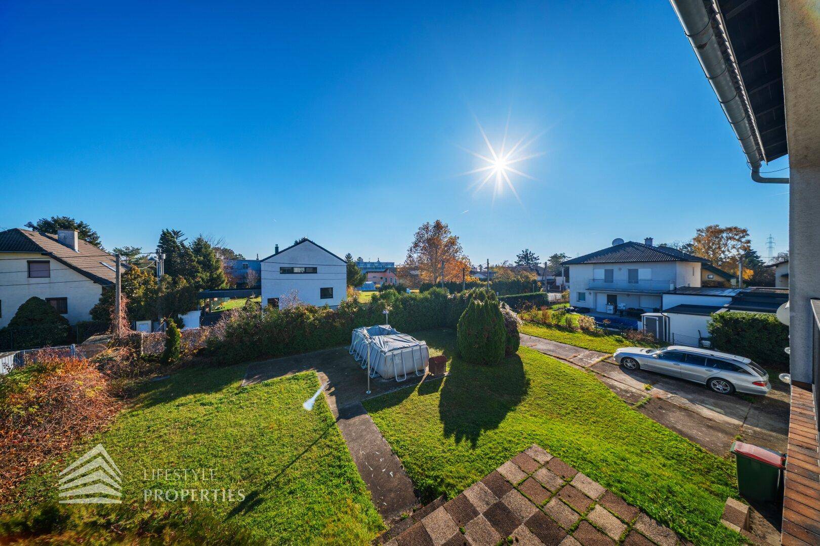 Balkonblick auf den Garten mit Pool und die umliegende Wohngegend.