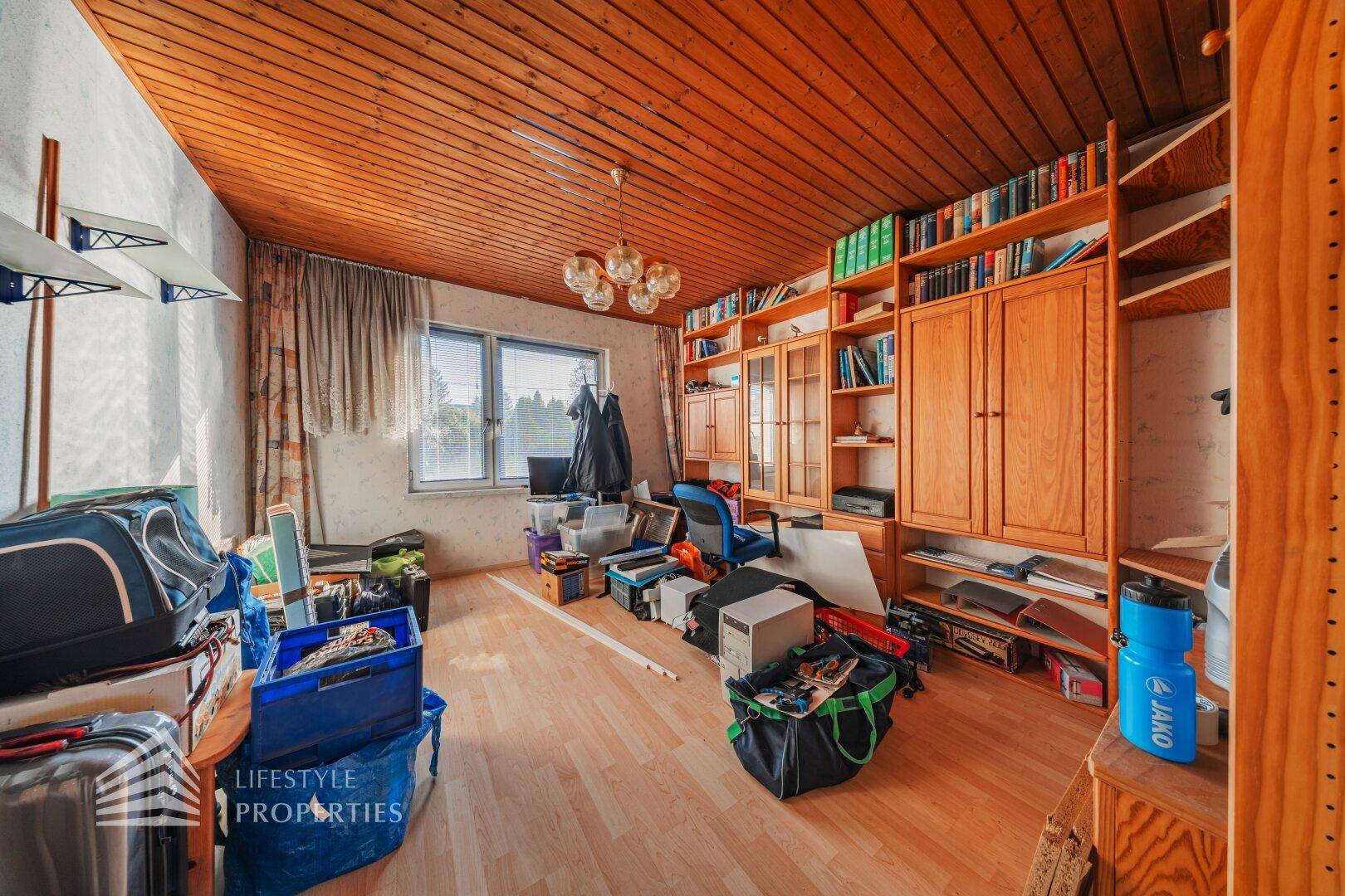 Arbeitszimmer mit Holzdecke, Laminatboden und vielen Bücherregalen.
