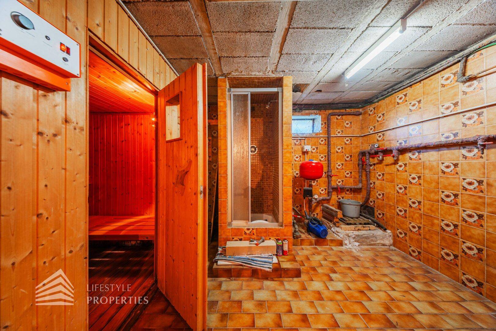 Hauswirtschaftsraum mit Dusche, Zugang zur Sauna und gefliesten Wänden.