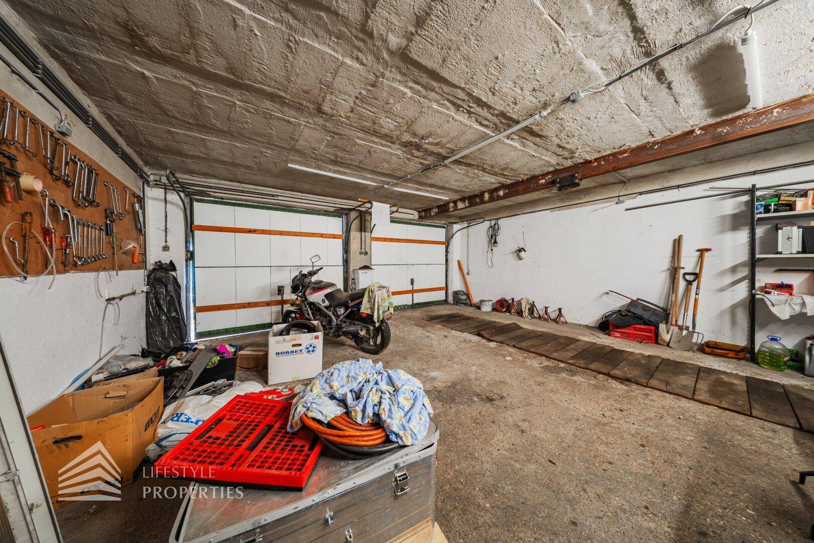Geräumige Garage mit zwei Toren, Betonboden und viel Platz für Werkzeuge.