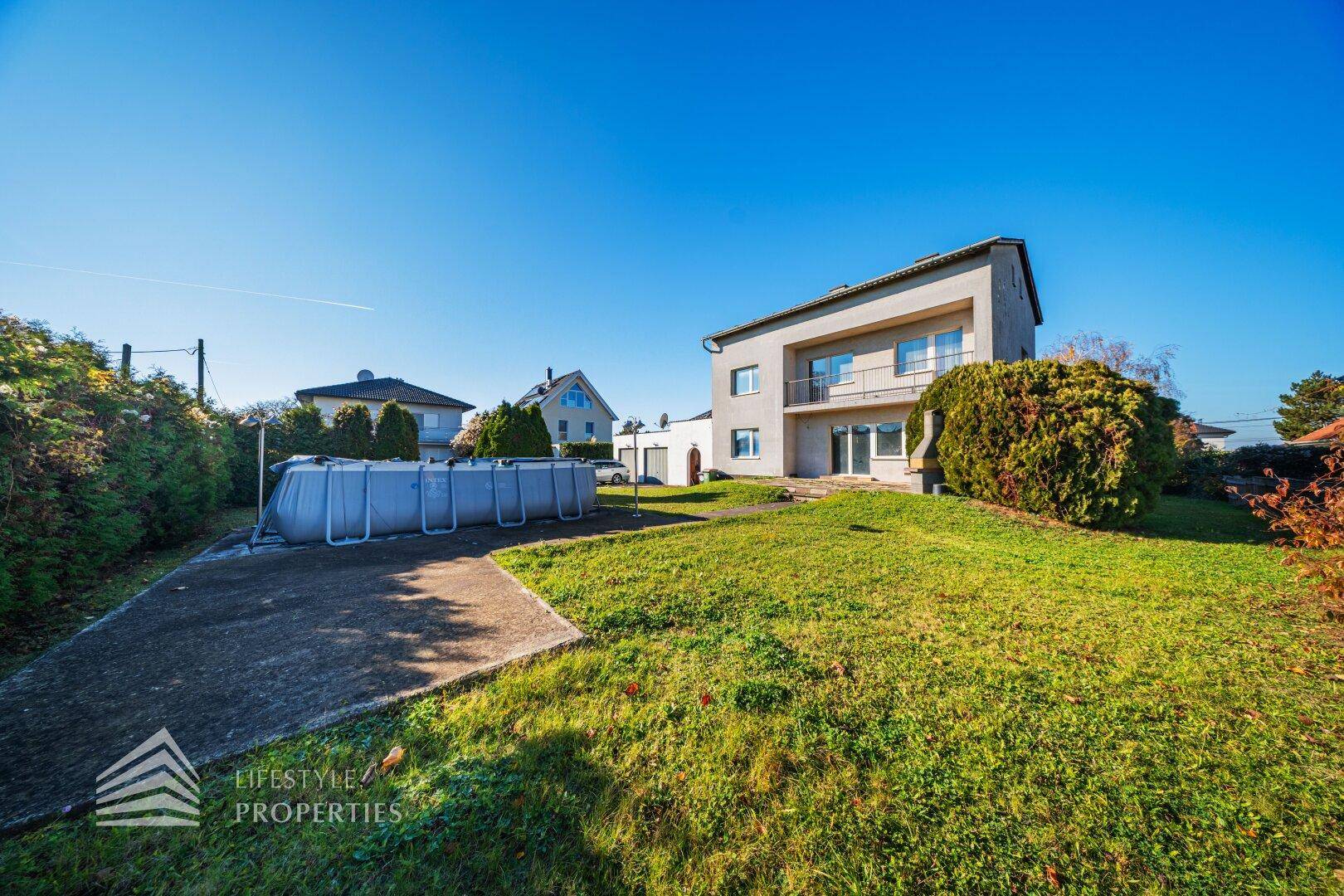 Seitenansicht des Hauses mit großem Garten und einem Aufstellpool unter blauem Himmel.