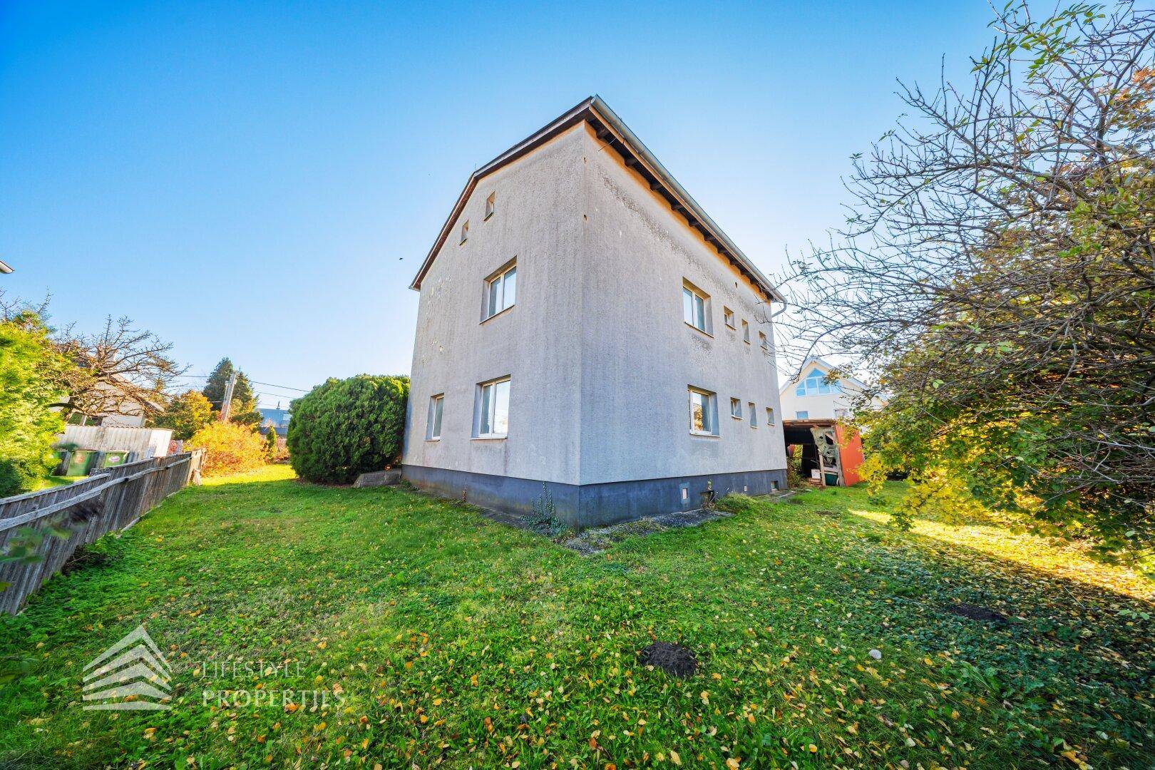 Seitenansicht des Hauses mit einfacher Fassade und umliegender Rasenfläche.
