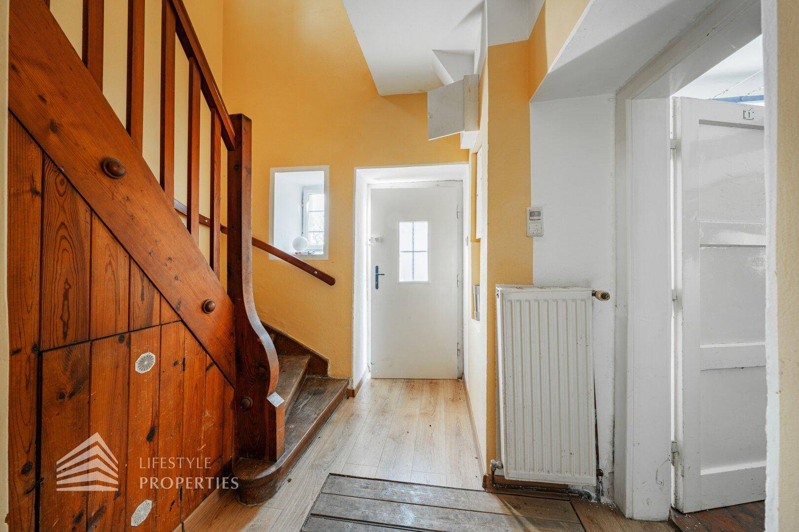 Heller Eingangsbereich mit Holztreppe, gelben Wänden und Holzboden.