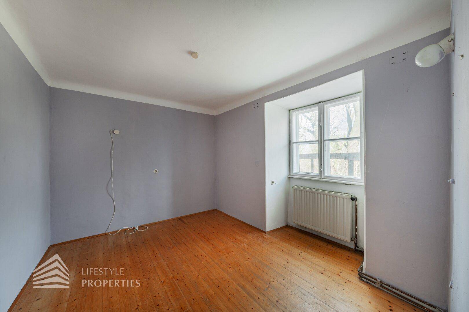 Helles Zimmer mit Holzboden, hellblauen Wänden und großem Fenster.