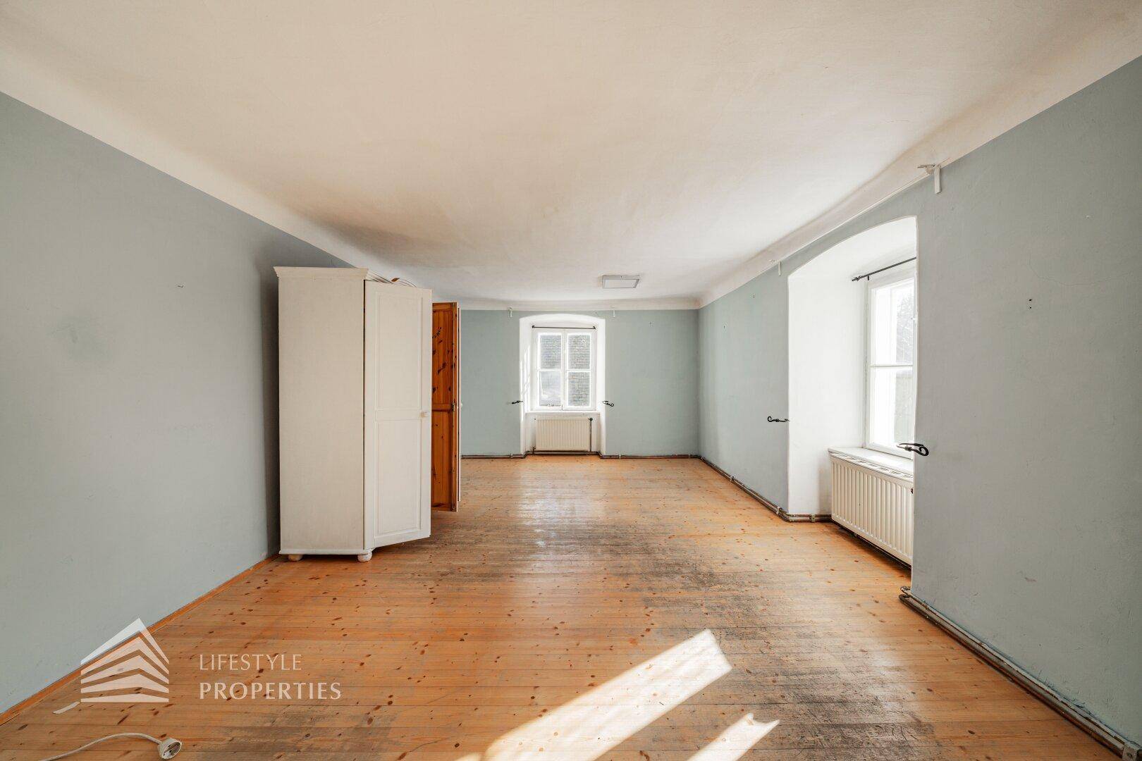 Geräumiges Zimmer mit Holzboden, hellblauen Wänden und mehreren Fenstern.