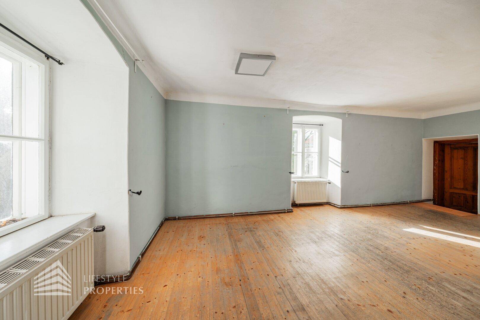 Helles Zimmer mit Holzboden, hellblauen Wänden und zwei großen Fenstern.