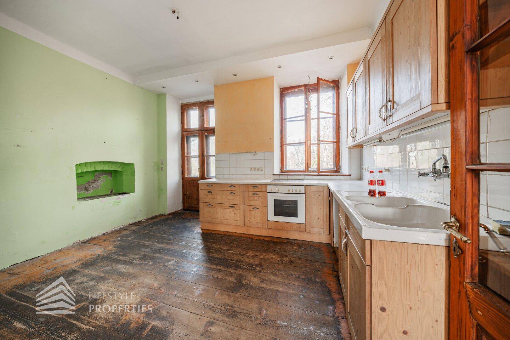 Küche mit Holzdielenboden, Holzschränken und grün gestrichener Wand.