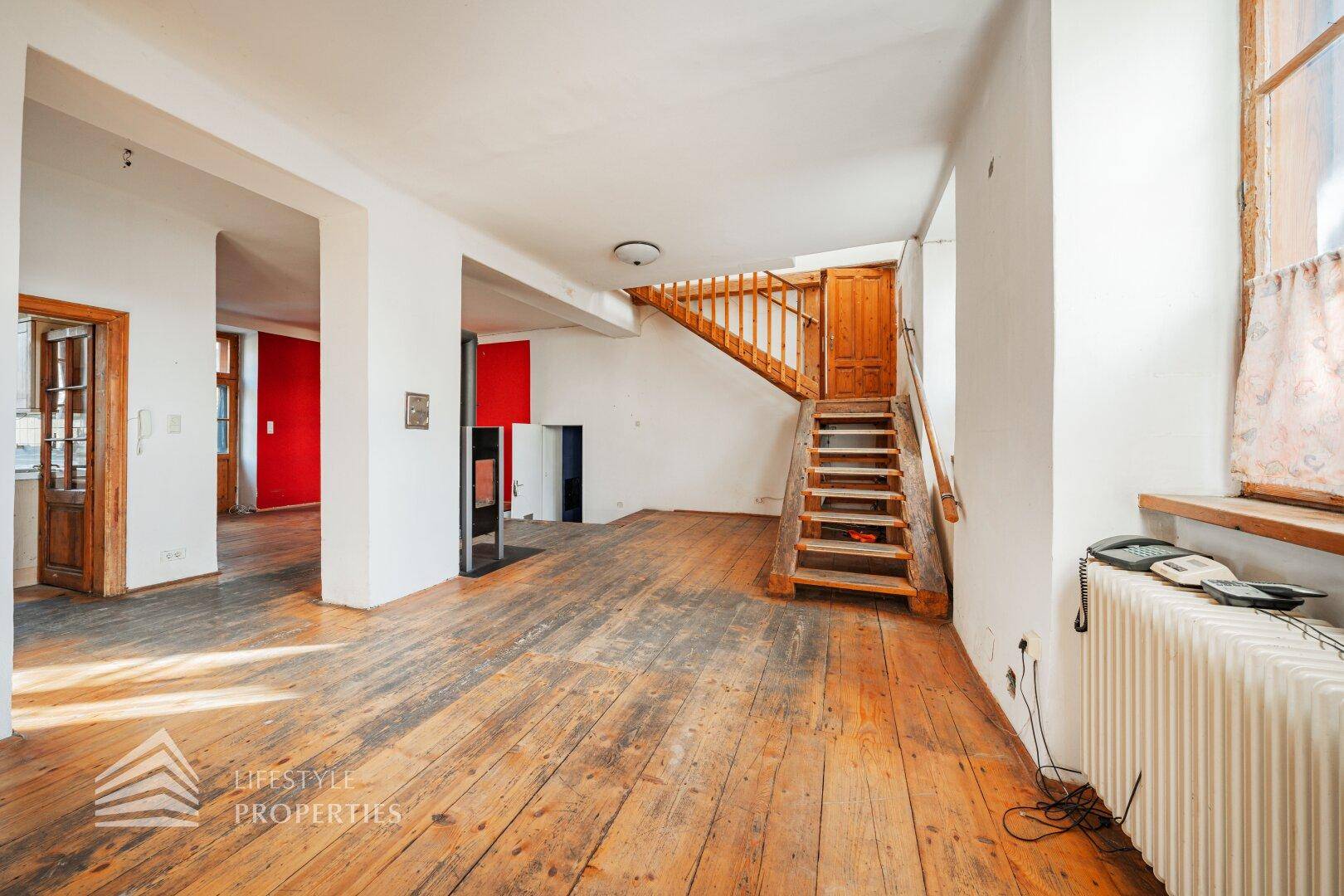 Offener Wohnbereich mit Holzdielenboden, Holztreppe und farbigen Wänden.