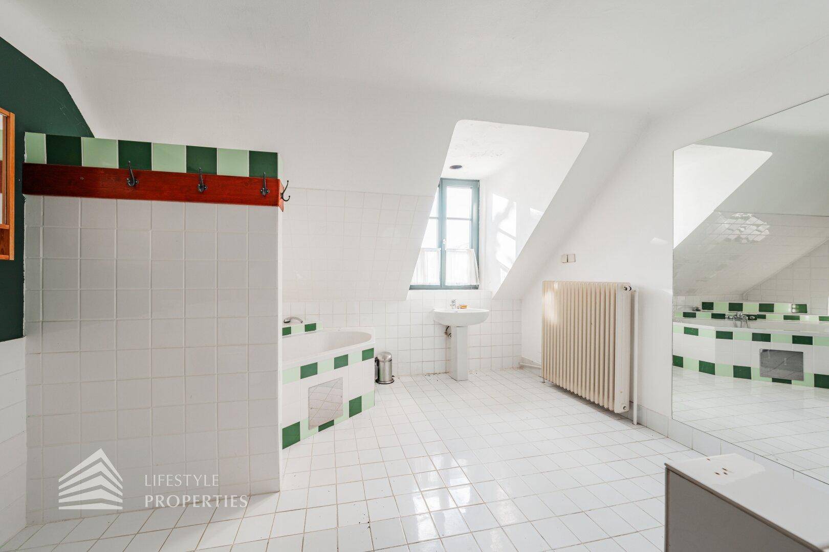 Geräumiges Badezimmer im Dachgeschoss mit Badewanne, weißen Fliesen und grünen Akzenten.